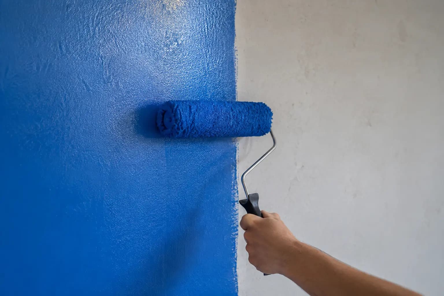 Persona pintando una pared con rodillo y pintura azul